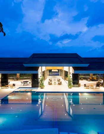 A luxurious building is lit up at night, featuring a large swimming pool reflecting the lights.