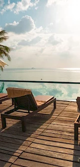 A serene poolside with lounge chairs, umbrellas, and a view of the ocean under a partly cloudy sky.