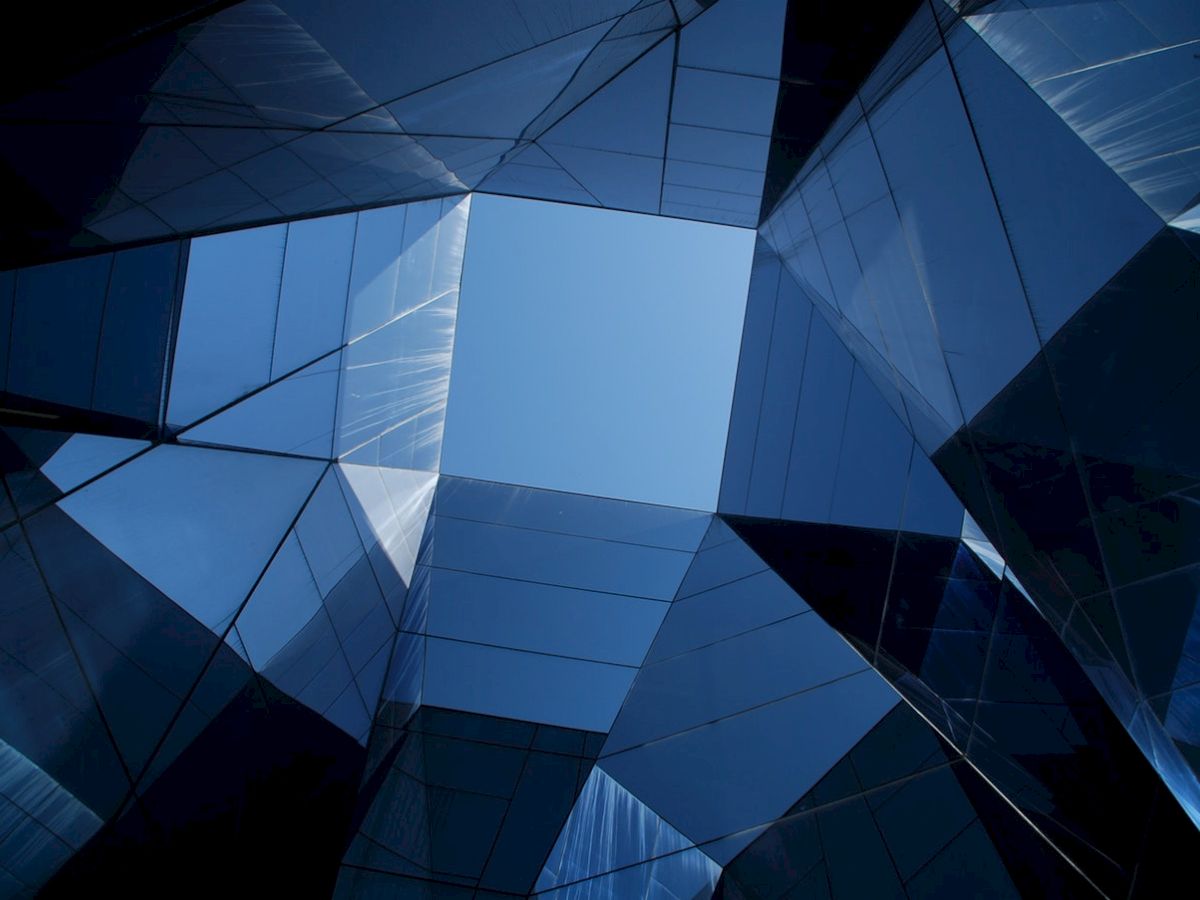 Geometric modern structures with reflective blue glass panels form a symmetrical view towards the sky.