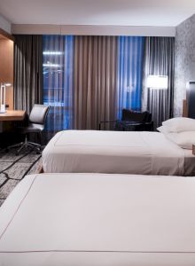 A modern hotel room with two beds, a wall-mounted TV, a desk, and ambient lighting.