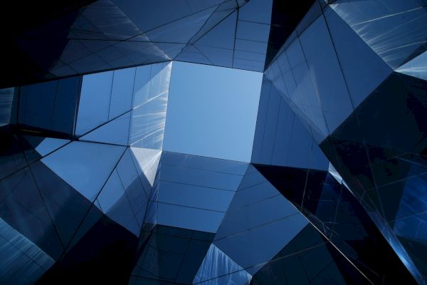 Abstract architectural design with reflective glass surfaces creating geometric patterns against a clear blue sky.