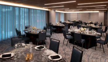 The image shows an elegantly set banquet hall with round tables, chairs, and decorative centerpieces, ready for a formal event.