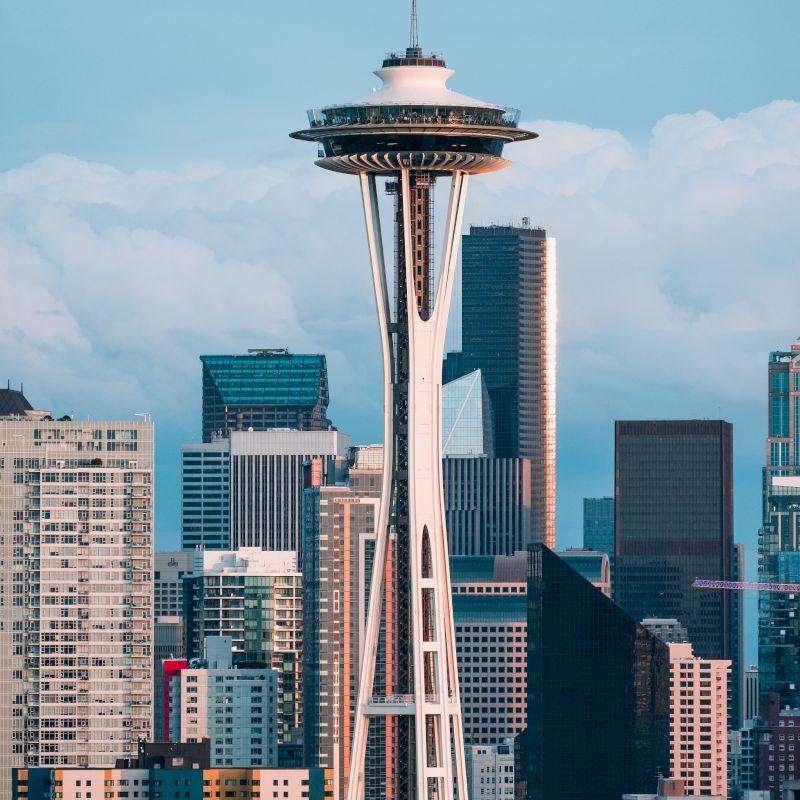 The image features the Space Needle against a backdrop of skyscrapers and a cloudy sky, depicting a cityscape view.