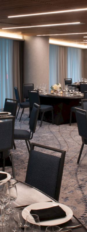 The image shows an elegantly set dining room with round tables, chairs, and decorative centerpieces, ready for an event or banquet.