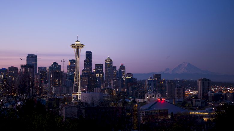 Seattle skyline at dusk with the Space Needle and Mount Rainier in the background, under a clear blue and purple sky.